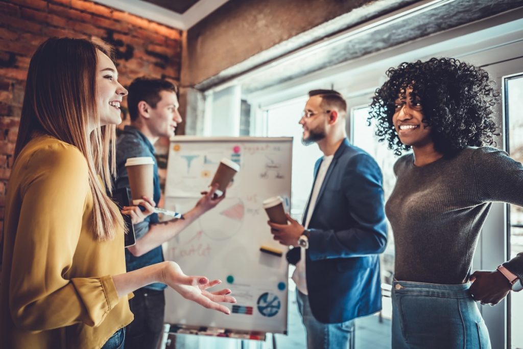 Pause for relax at work. Happy work team during break time in light modern office, talking, having drinks, smiling, all dressed in casual outfits.